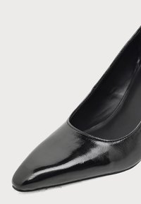 Gros plan sur une chaussure à talon haut en cuir verni noir à bout pointu avec une finition lisse et brillante.