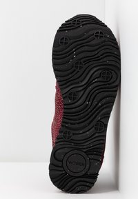 Semelle de chaussure avec une bande de roulement ondulée noire et des motifs circulaires, tige en tissu bordeaux et logo "WODEN" embossé près du talon.