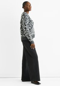 Grauer und weißer Leopardenmuster-Pullover mit gerippten Bündchen und Saum, kombiniert mit hochgeschnittenen schwarzen weit geschnittenen Jeans und flachen schwarzen Schuhen.