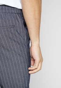 Szare spodnie w prążki z elastycznym pasem. Tkanina ma fakturę, z bocznymi kieszeniami i prostymi nogawkami.