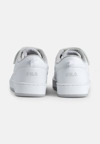 Valkoiset nahkakengät, joissa on teksturoitu pinta, litteät valkoiset pohjat ja vaaleanharmaat yksityiskohdat. Varustettu tarranauhalla ja kohokuvioidulla logolla kannassa.