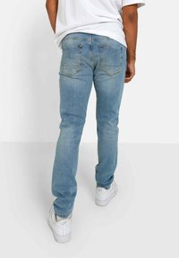 Vaqueros de mezclilla azul claro con un ajuste slim, que cuentan con bolsillos traseros y sutiles detalles de costura. Llevados con zapatillas blancas.