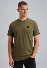 Olijfgroen katoenen t-shirt met korte mouwen, ronde halslijn en een klein bruin label op de borst. Zachte textuur, ontspannen pasvorm.