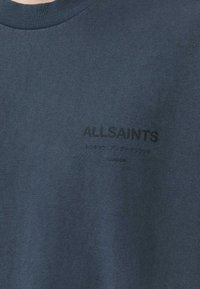 Dark blue cotton t-shirt features a crew neck and a printed logo in black, positioned centrally with additional text underneath.