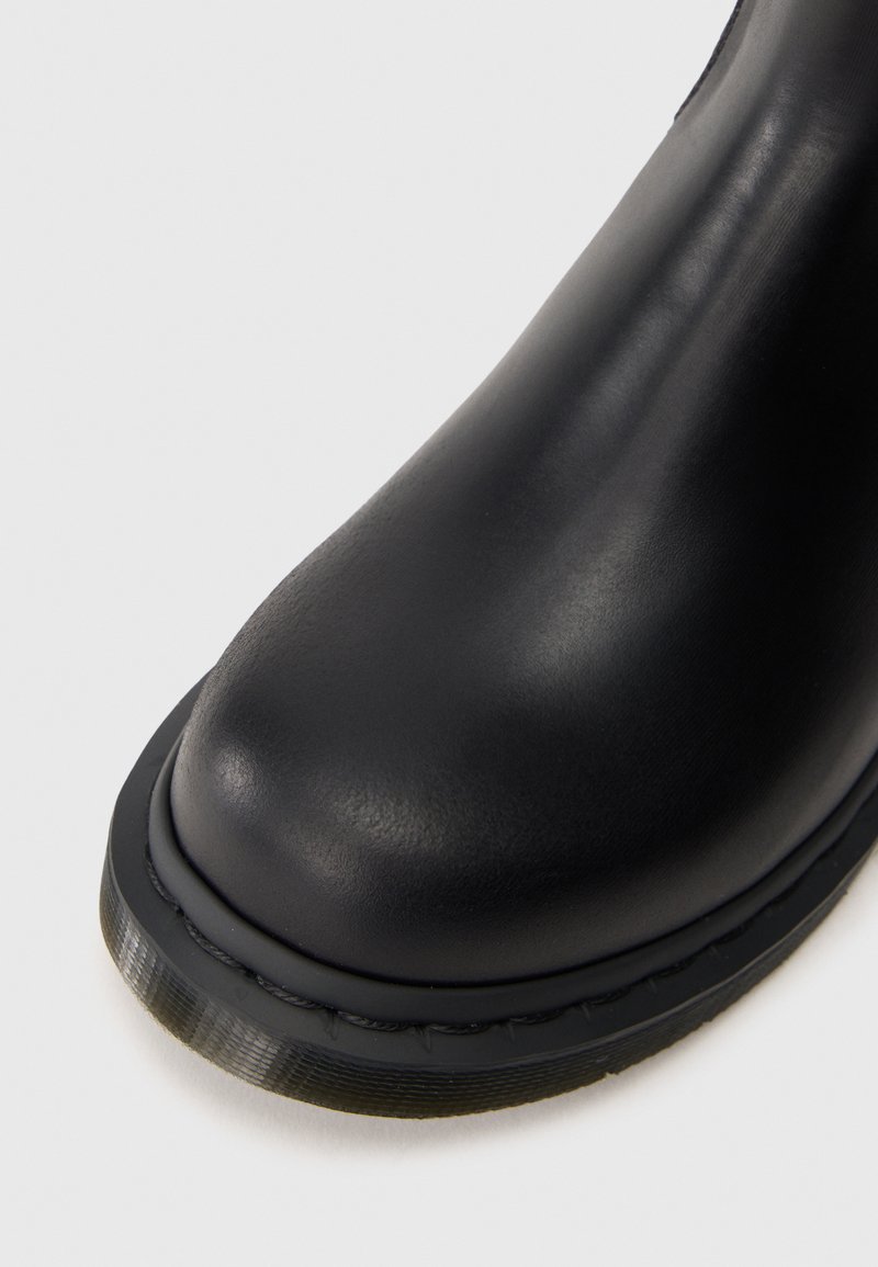 Puntera de bota de cuero negro con suela gruesa cosida sobre un fondo blanco.