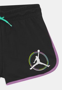 Pantalones cortos de baloncesto negros con ribete púrpura, con un logotipo blanco de Jumpman dentro de un círculo multicolor. Cintura elástica con cordón turquesa.