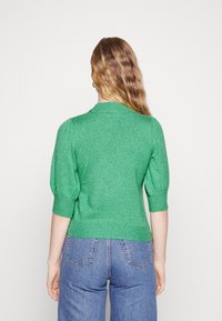 Groene gebreide trui met een geribde kraag, korte pofmouwen en een aansluitende taille. Gecombineerd met lichtblauwe high-waisted jeans.