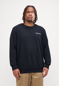 Czarny sweatshirt z okrągłym dekoltem wykonany z miękkiego materiału, z białym haftem "Club1990" po lewej stronie klatki piersiowej, luźny krój i długie rękawy.