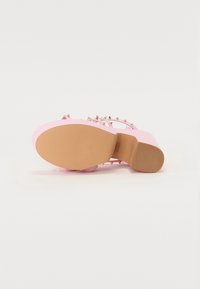 Rosa plattform sandal med gullpigger på stropper. Flat såle med teksturert grep. Glatt overmateriale, avrundet tåform.