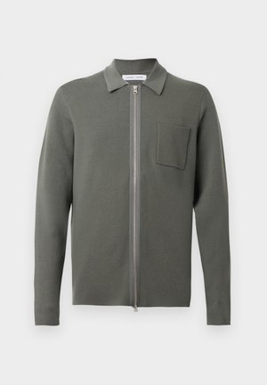 Olivengrønn cardigan med glidelås foran, lange ermer, en liten brystlomme og en strukturert strikket finish. Minimalistisk design.