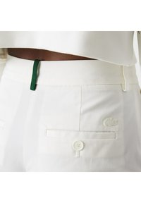 Pantalon blanc avec un accent vert à la taille, deux poches avant, une fermeture à bouton et un logo brodé.