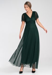 Langes grünes Kleid aus fließendem Material, mit kurzen, transparenten Ärmeln, einem V-Ausschnitt und einer taillierten Taille, sowie einer glatten, geschichteten Textur.