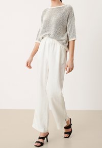 Lätt, stickad tröja i krämfärg och svart, kombinerad med vita linnebyxor. Outfiten kompletteras med svarta remsandaler.