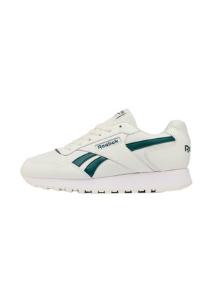 Witte Reebok sneaker met donker groene zijstrepen, vetersluiting en een logo van het merk op de zijkant en hiel, gezien vanaf de buitenkant.