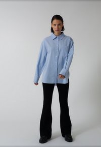 Světlomodrá košile na knoflíky s límečkem a svislými pruhy. Má kapsu na prsou. Kombinována s černými rozšířenými kalhotami a robustními botami.