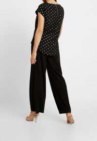 Top nero con pois bianchi, maniche corte e orlo arrotondato, abbinato a pantaloni neri a gamba larga e décolleté beige con cinturini.