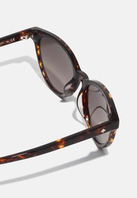 Óculos de sol redondos com armações de plástico em padrão tartaruga escura, lentes degradadas e detalhes em tom dourado nas dobradiças.