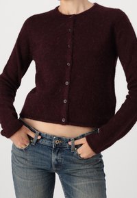 Vinröd kort kofta i mjukt tyg med långa ärmar och sex mörka knappar, kombinerad med ljusblå denimjeans.