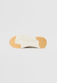 Sohle eines Sneakers mit einem geriffelten Design in Beige und Creme, das eine strukturierte Oberfläche und einen glatten weißen Gummibereich aufweist.