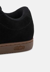 Svart semsket sneakers med avrundet form, featuring en gummisåle og teksturerte detaljer. Merkevaren "etnies" er preget på hælen.