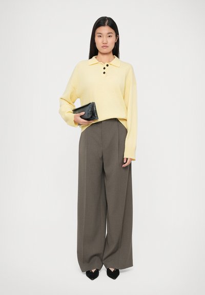 Maglione polo in maglia gialla con tre bottoni, abbinato a pantaloni grigi con gamba larga e vita alta. Tiene una piccola pochette nera testurizzata.