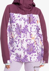 Lila och vit blommig jacka med enfärgade lila ärmar och bröst, framtida dragkedjeficka, bärs med ljuslila byxor med en dragkedjeficka.