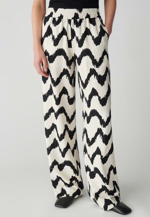 Losse zwart-wit zigzag broek met elastische tailleband, gedragen met een zwart topje en zwarte schoenen met een vierkante neus.