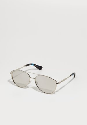 Óculos de sol com armação de metal e um acabamento prateado subtil. Lentes ovais em cinza claro, apresentando hastes finas com um padrão azul e preto nas pontas.