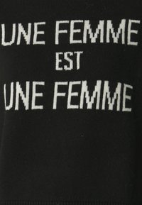 Maglione nero con testo bianco lavorato a maglia: "UNE FEMME EST UNE FEMME." Testo disposto in un formato impilato sulla stoffa.