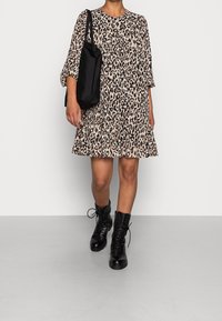 Robe à imprimé léopard avec un ourlet volanté, manches trois-quarts, associée à un sac fourre-tout noir et des bottes de combat noires à lacets.