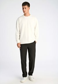Felpa bianca con colletto a girocollo e maniche lunghe, abbinata a pantaloni neri e sneaker bianche; texture liscia, vestibilità rilassata, design minimalista.