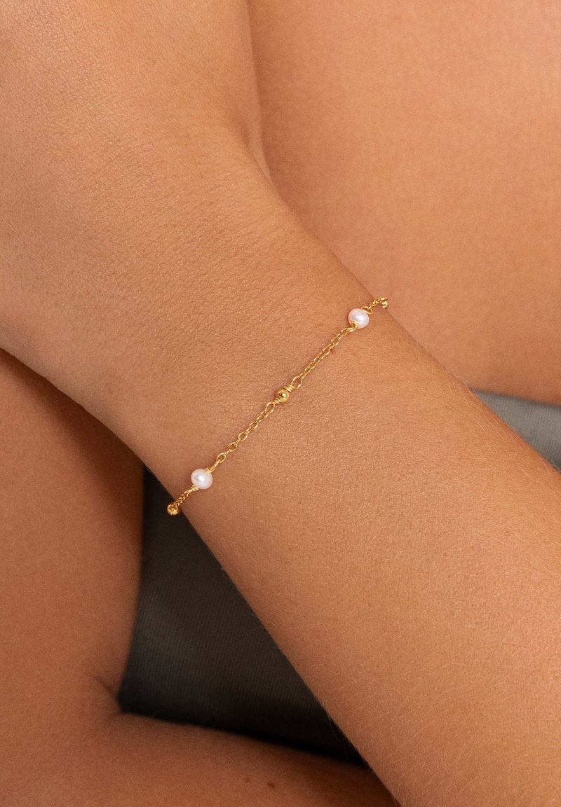 Bracelet en chaîne dorée avec trois petites perles, présentant un design délicat et de fins maillons sur un fond de peau bronzée.
