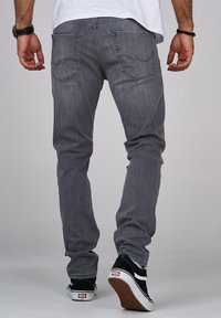 Jeans in denim grigio con vestibilità slim, dotati di tasche posteriori e dettagli di cucitura sottili. Indossati con sneakers nere con accenti bianchi.