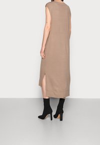 Abito lavorato a maglia beige con una vestibilità ampia, spacchi laterali, maniche corte e scollo rotondo, abbinato a stivaletti neri con tacco alto.