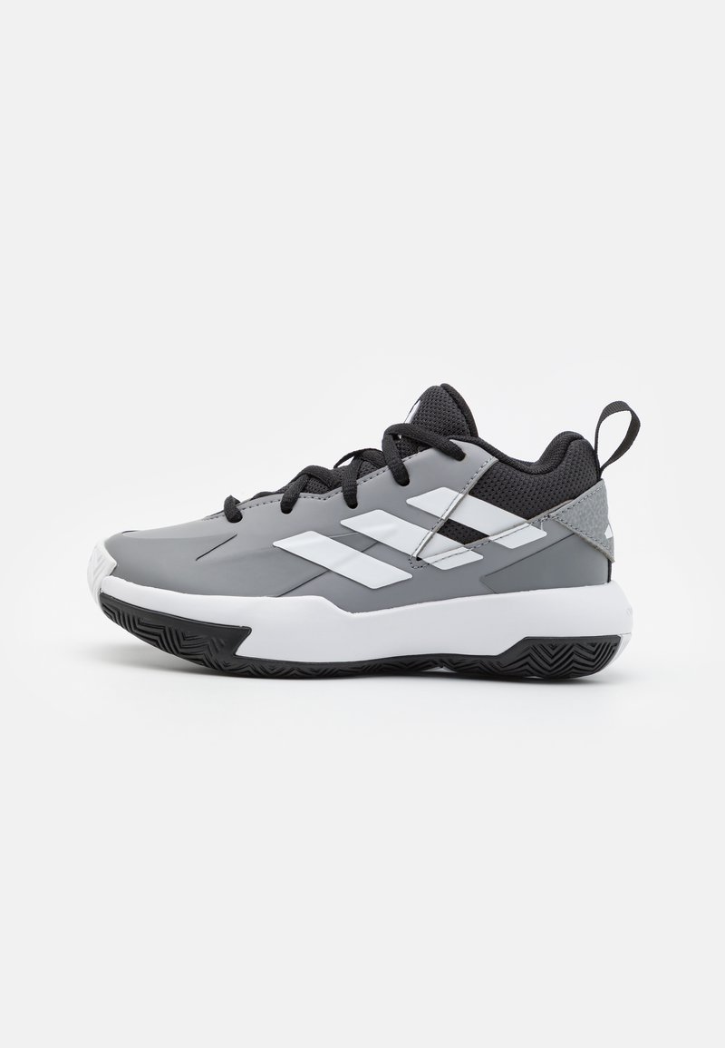 Chaussures de sport grises avec des accents blancs, présentant une tige synthétique texturée, des lacets noirs et une semelle en caoutchouc avec un motif pour une meilleure adhérence.