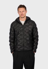 Sort pufferjakke med en tekstureret overflade, der har lynlås foran, hætte og sidelommer. Lavet af letvægtsmateriale.