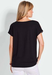 Zwart T-shirt met korte mouwen en een losse pasvorm, voorzien van kleurrijke accenten op de schouders en een ronde halslijn. Zachte stof met een gladde textuur.
