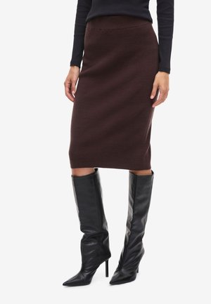 Falda midi de punto acanalado en marrón, diseño ajustado, combinada con botas de piel negras de tacón stiletto hasta la rodilla, creando una silueta elegante.