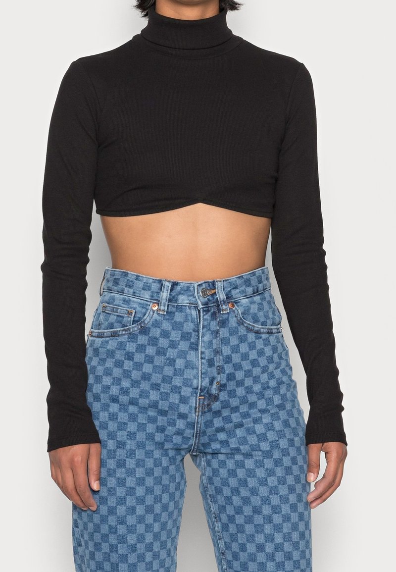 Svart kortärmad turtleneck-top med långa ärmar, parat med högmidjade blå rutiga jeans som visar en slät textur och figurnära design.