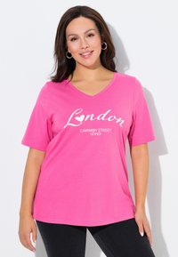 Maglietta di cotone rosa con maniche corte e scollo a V. Presenta una scritta bianca stampata "London Carnaby Street Soho" sulla parte anteriore.