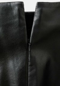 Prenda de cuero negro con una textura suave y costuras visibles, que presenta un cierre central con cremallera para mayor funcionalidad.