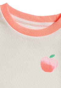 Tissu côtelé blanc avec un col rond couleur pêche ; présente un design imprimé de pomme en rose et vert sur le côté gauche.