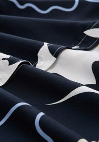 Tissu textile avec une base bleu marine et des motifs abstraits blancs et bleu clair. Texture douce avec des détails en boutons cousus le long du bord.