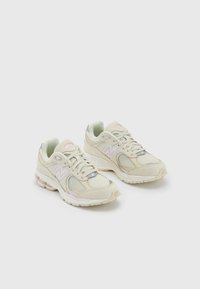 Beige mesh sneakers with light gray accents, textured surfaces, rounded toe, and cushioned sole featuring a subtle pink stripe and logo.