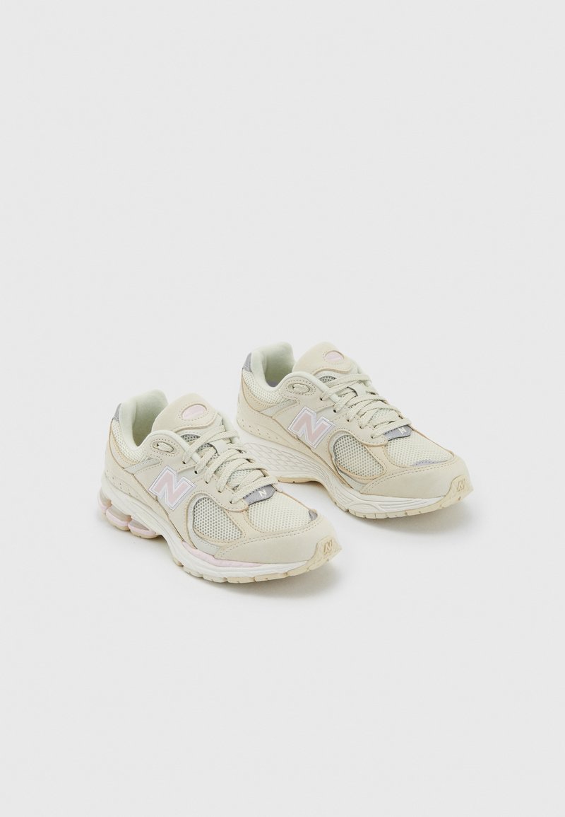 Beige mesh sneakers with light gray accents, textured surfaces, rounded toe, and cushioned sole featuring a subtle pink stripe and logo.