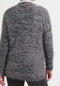 Tjock grå tröja med en texturerad stickning, med en lös passform och längre baktill. Designen innehåller subtila silvertrådar för kontrast.