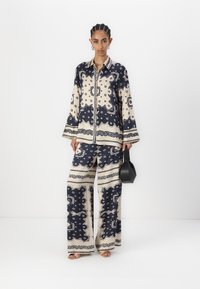 Navy and cream patterned two-piece outfit featuring a long-sleeve shirt and wide-leg pants, with paisley designs and a button closure.