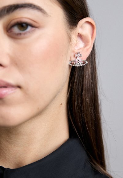 Brincos de prata com um design de cruz, adornados com pedras preciosas rosa e transparentes, com um trabalho em metal intricado e um detalhe de argola circular.