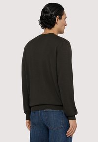 Mörkgrön tröja med ribbad krage och manschetter. Har en jämn textur och en klassisk rund halsringning, i kombination med blå denimjeans.