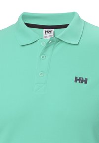 Polo de color verde claro hecho de tejido texturizado, con una tapeta de dos botones y un logo en navy en el lado izquierdo del pecho.